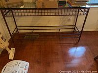 Full view of the metal framed glass table showing grid design on sides and open lower section, on hardwood floor near wall.