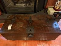 Top angled view of the rectangular wooden trunk showing wood grain, metal hinges, latch and top surface wear.