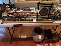 Photo of walking cane, tribal wind instrument, and gong with stand arranged on folding table alongside other miscellaneous items.