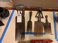 Five wooden hair picks from the South Pacific arranged on a table, showing various carved human figures and intricate patterns on the picks.