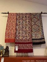 Front view of three decorative fabric wall hangings displayed on black metal rod with finial ends, visible full length drape and patterns