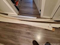 Fourteen white baseboard boards stacked on floor near doors, showing length and quantity.