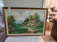 Full frontal view of the framed oil on canvas painting showing the English cottage in a lush countryside setting.