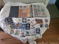 Full view of baseball cards and souvenir schedules laid out on a table, binder containing baseball cards open with visible cards inside, and multiple souvenir schedules spread out.
