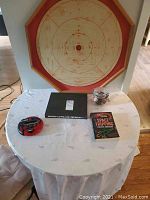 Full view of the wooden Crokinole board hanging on wall behind a table that holds the books, game, and playing pieces in a jar.