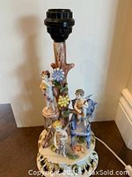 Full view of porcelain table lamp showing detailed putti angels and floral decorations with lamp socket on top