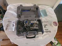Dremel Trio rotary tool in carrying case with power cord and paperwork spread on table