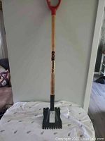 Full view of Garant roofing shovel standing upright showing wooden handle with red D-shaped grip and black metal blade.