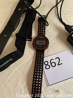 Garmin Forerunner 220 watch with black perforated silicone strap, adjustable Garmin heart rate monitor strap, and charging cable laid out on light background.