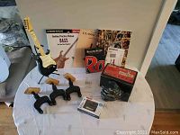 Wide photo of all items on round table including guitar, practice books, Rolling Stone DVD set, guitar wall mounts, Guitar Grip hand mount, microphone, and music bank.