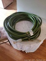 Coiled green heavy-duty garden hose on a white surface indoors for a clear overview.