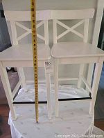 Two white IKEA INGOLF high-top chairs with a tape measure showing seat height approximately 26 inches.