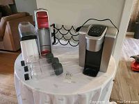 Full view of the lot on a round table showing SodaStream, Rival popcorn popper, Keurig coffee maker, and wine racks