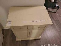 Front view of off-white cabinet with 2 doors and 2 drawers, showing wear on the tabletop.