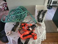 Full view of orange Norguard safety harness, green rope coiled on table, and white bucket in background