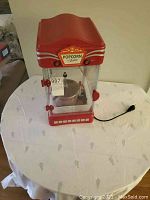 Full view of the red and clear plastic electric popcorn machine on a table