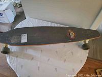 Top side of the longboard showing black grip tape with Sector 9 sticker and worn surface.