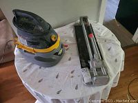 Stinger wet/dry vac and tile cutter on round table covered with white sheet showing both items together.