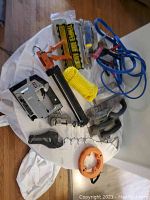 Various tools including Porter Cable crown stapler, booster cables, yellow rope, roof anchor clamp, and other hand tools arranged on a white surface