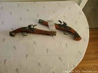Two replica vintage flintlock pistols laid out on a white tablecloth, showing overall shape and design.