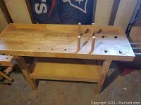 Front view of full woodworking bench showing top, bench dogs, and frame with lower shelf