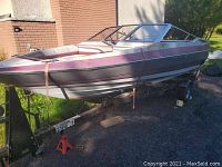 Side view of burgundy and white fiberglass bowrider boat mounted on black tilt trailer
