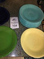 Set of 11 Fiesta Ware plates in turquoise, yellow, cobalt blue, shamrock green, and tangerine orange colors arranged on a countertop.