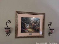 Framed print of Thomas Kinkade's "Hidden Cottage" with two matching wall sconces mounted on wall.
