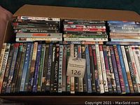 Photo showing multiple DVDs stacked and organized on a cardboard box. Titles on DVDs include Yours, Mine & Ours, Bourne Supremacy, Harry Potter and other assorted genres.