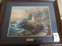 Full view of framed artwork depicting lighthouse, ocean and cottage scene in pastel tones.