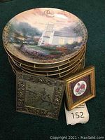 Stack of 10 collector plates with scenic art including a church, metal engraving with peacock and floral border, and small framed floral art.