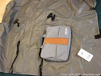 Full view of gray KURGO Wander Hammock car seat cover spread out with attached storage pouch with orange dog pattern strip and buckles and straps visible.