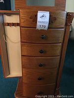 Front view of the jewelry armoire shows the five drawers, carved accents, and the side doors with necklace hooks.