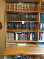 Full book lot displayed on wooden shelves plus a table below, showing multiple volumes of Bible study commentaries, textbooks, and cookbooks.