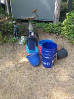 Overview of blue plastic buckets including a Lowe's branded bucket, assorted pots and some yard accessories placed on grass.
