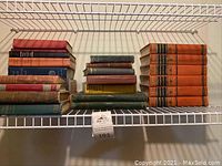 Overall view of assorted books on a metal shelf, including different sizes and colors, with large set of orange Abraham Lincoln encyclopedias visible on right side.