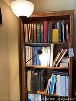 View of wooden bookcase with various books on top shelves and black floor lamp on left side