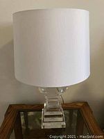 Full view of the table lamp showing white fabric shade and clear glass base on wooden surface.
