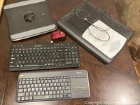 Photo of two wireless keyboards, a red wireless mouse, and two laptop cooling pads placed on a wooden table.