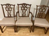 Three antique wooden dining chairs seen from front showing carved backs and cream upholstered seats. Two are armless and one with arms.