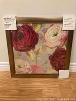 Front view of the framed floral Wall Art with tags visible, showing red, pink, and cream flowers with green leaves and gold accents, set in a gold frame.