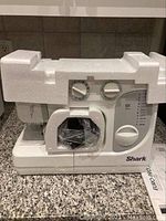 Front view of the white Shark sewing machine with visible stitch selection dials and protective styrofoam on top.