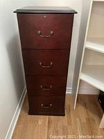 Photo of a tall wooden filing cabinet with four drawers and metal handles on each drawer. The top drawer has a lock.