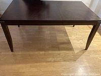 Full view of the rectangular wooden dining table showing front and side, dark finish, four angled tapering legs.