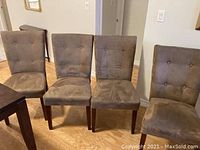 Four brown upholstered dining chairs with button-tufted backs and wooden legs, arranged in a row on light wood flooring. Chairs show visible dirt and wear.