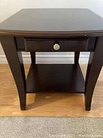 Front view of the dark wood side table showing drawer and lower shelf against hardwood floor.