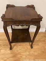 Full view of the antique wooden side table showing carved edges and legs, overall vintage condition with wear visible.