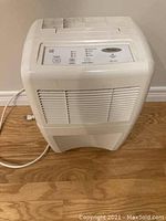 Front angled photo of white Whirlpool dehumidifier unit on wood floor, showing front vent and control panel.