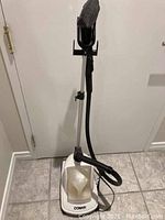 Full view of the Conair garment steamer showing the main base with water reservoir, black hose, adjustable metal pole, and the steam head on top.