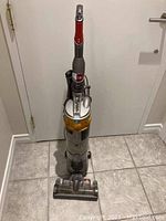Front view of silver and yellow Dyson upright vacuum with red accents, hose and wand attached